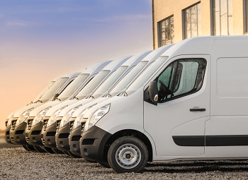 Several white commercial vans parked in a row in a parking lot