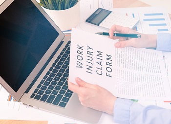 person holding a work injury claim form in their hands in front of a laptop